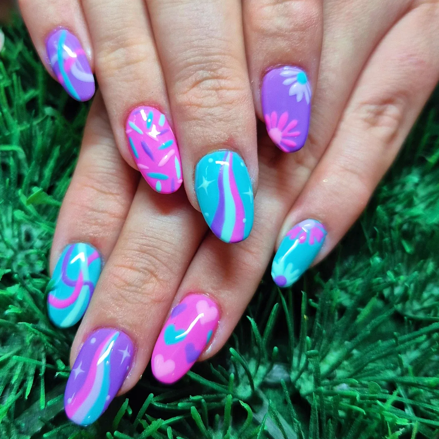 These long, almond-shaped nails are painted in bright turquoise, hot pink, and purple. Each nail features a mix of bold stripes, swirls, hearts, flowers, and star accents, with glossy finishes throughout. The designs vary from nail to nail, creating a playful, mismatched look with strong 90s and retro pop-art vibes. This vibrant, colourful manicure feels fun and expressive, making it a perfect choice for summer, festivals, or any time you want statement nails that stand out.