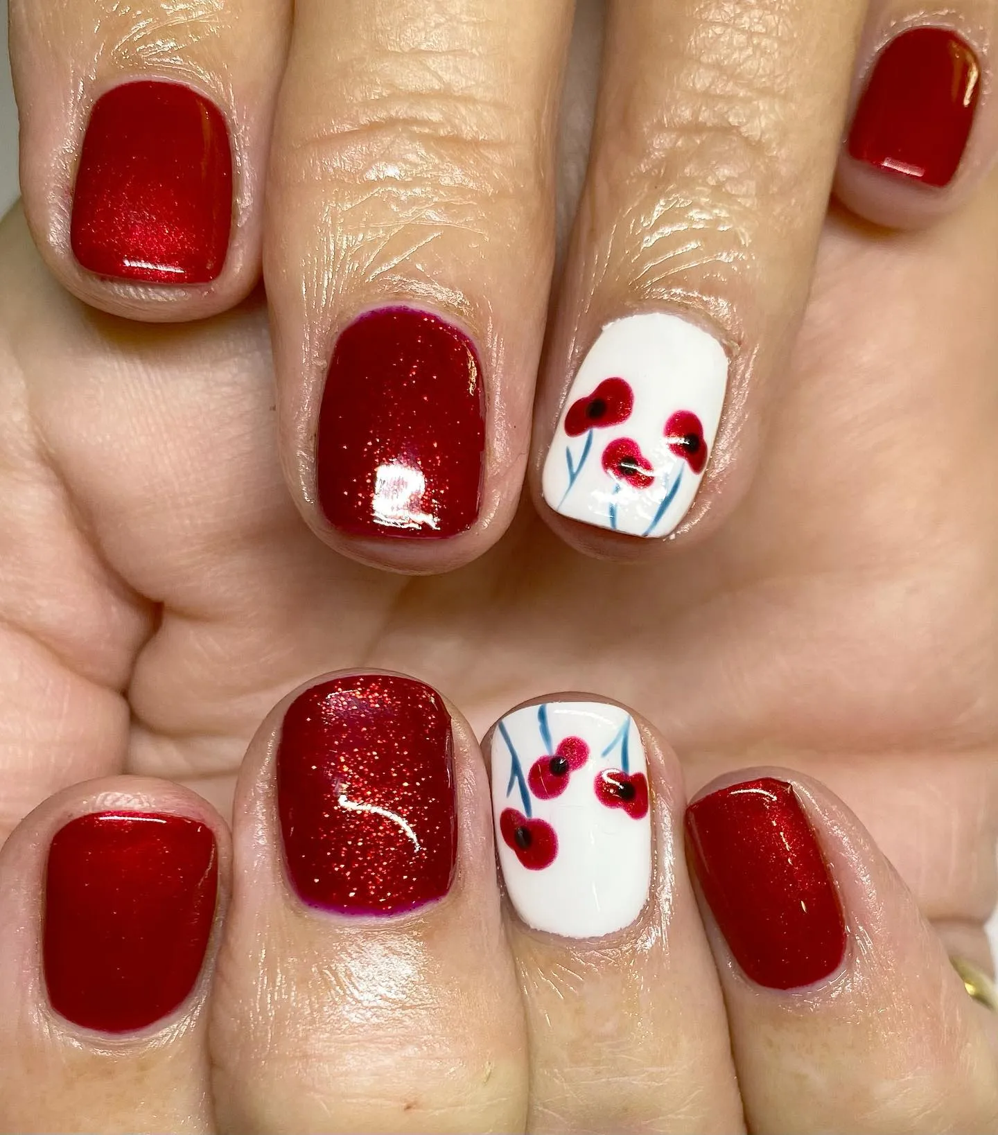 Simple yet striking — rich, glossy red nails paired with a crisp white accent nail featuring minimalist poppy stems. A sweet and wearable design that still carries a powerful message of remembrance. Created by @simply_chic_nails_by_bekki.